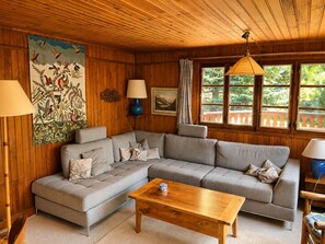 Un salon chaleureux avec un canapé d’angle, une table basse en bois et une grande fenêtre donnant sur un paysage verdoyant.