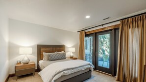 A bedroom with a large bed, two bedside tables with lamps, a wooden headboard, and a view through a sliding glass door to an outdoor area.