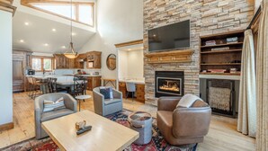 A spacious living area with a fireplace, comfortable seating, and a kitchen in the background.