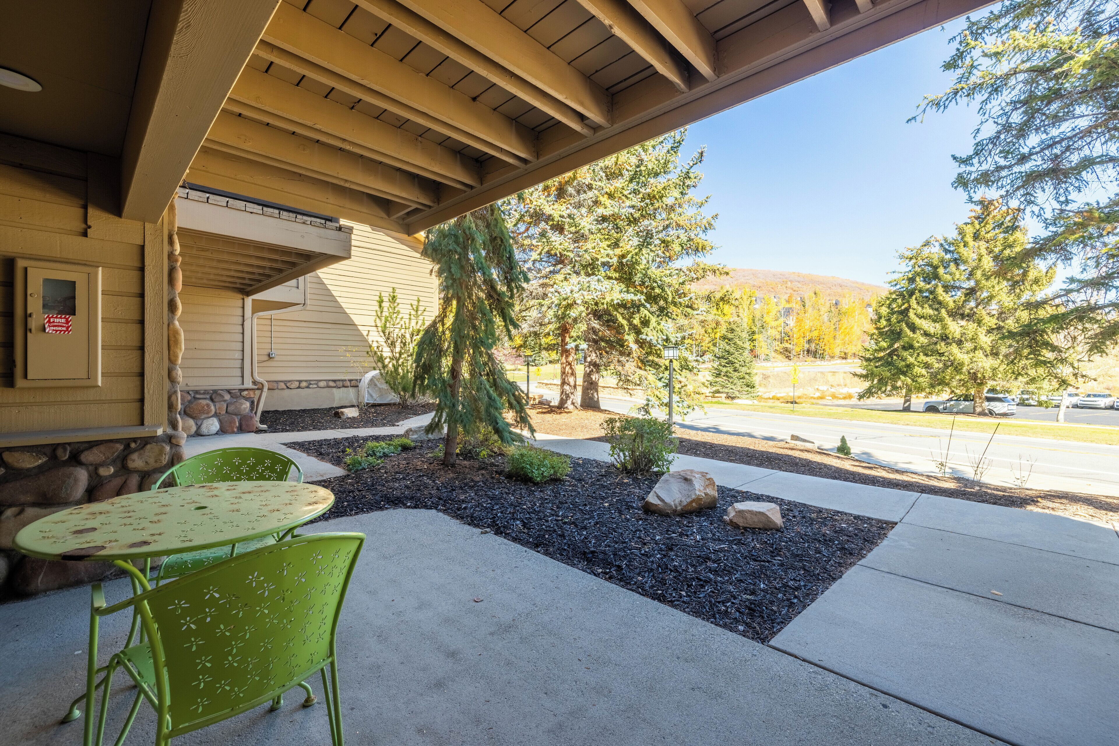A covered patio with a table and chairs, a small tree, and a stone wall.