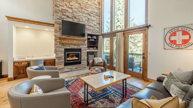 A living room with a stone fireplace, leather sofas, a flat-screen TV, and a ski patrol sign on the wall.