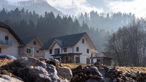 Een rij huizen met een berg op de achtergrond, een heldere lucht en een rotsachtige voorgrond.