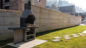Een betonnen buitenbarbecue met schoorsteen, een bakstenen gebouw op de achtergrond en een heldere lucht.