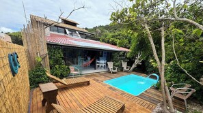 A wooden deck with a pool, outdoor furniture, and a covered patio area.