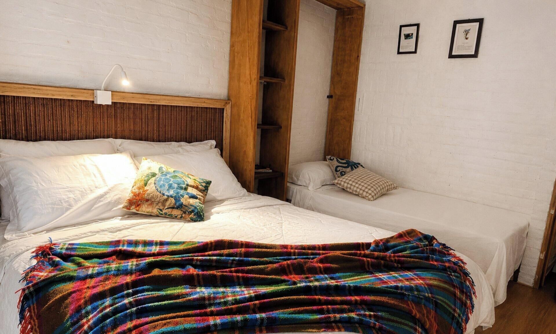 A bedroom with a bed, a bench, and a wall with two framed items.