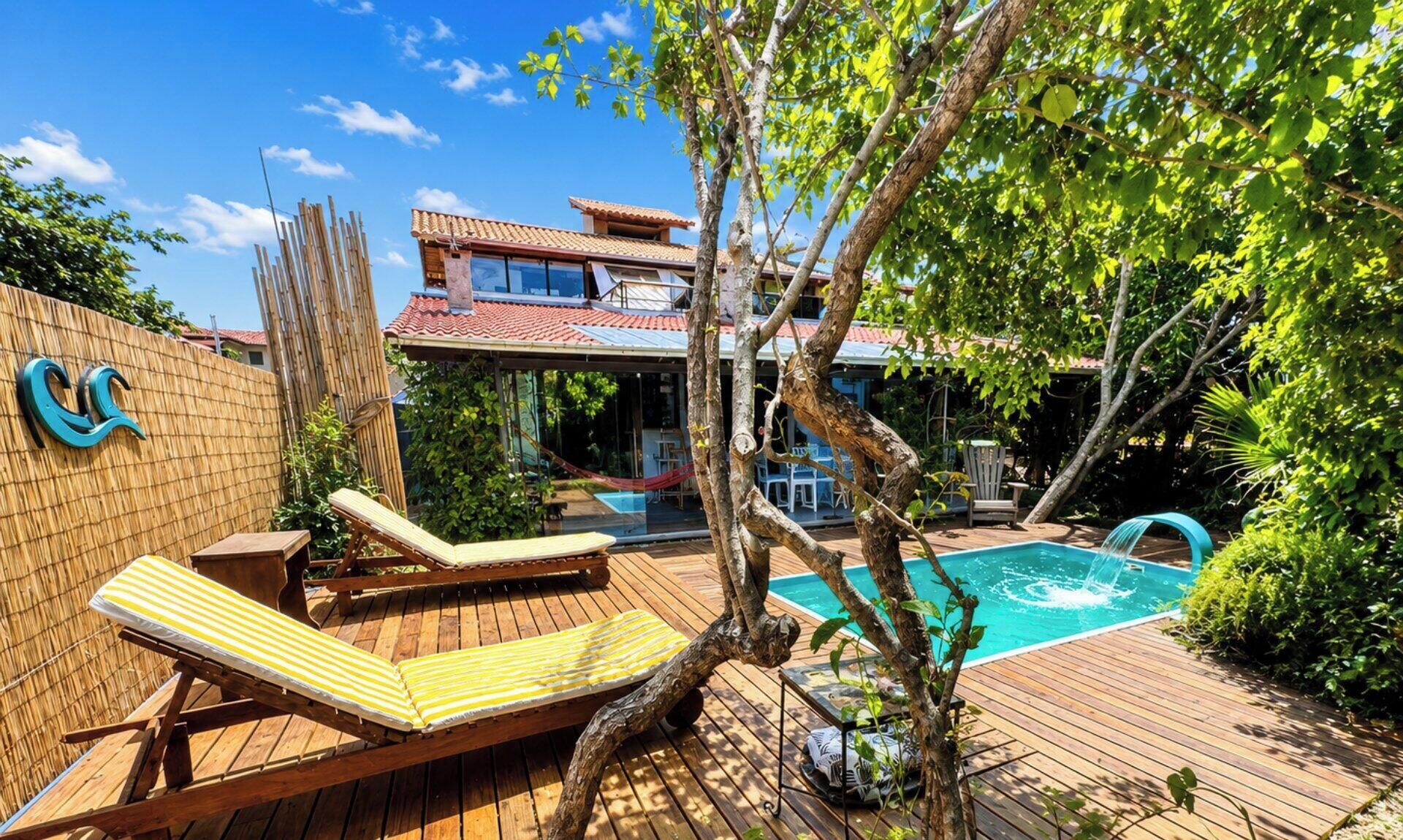 A wooden deck with two sun loungers, a swimming pool, and a bamboo fence.