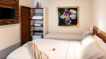 A hotel room with two beds, a flat-screen TV mounted on the wall, a shelf with folded towels, and a painting on the wall.