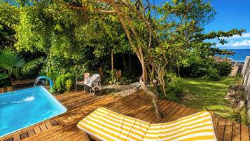 Une terrasse en bois avec une piscine, une chaise longue et une table recouverte d’une nappe.