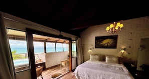 A bedroom with a bed, a painting, a chandelier, and a view of the ocean. - Pousada Ondas da Grande – Penha/SC (Penha)