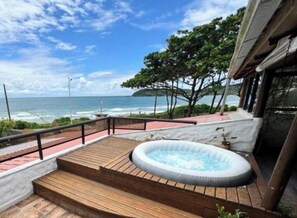 A wooden deck with a hot tub, a view of the ocean, and a tree-lined path.