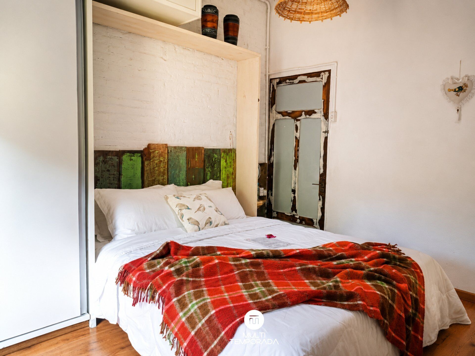 A bedroom with a bed, a wooden headboard, a mirror, and a door with peeling paint.