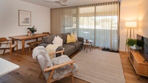 Ett modernt vardagsrum med en grå soffa, trämöbler, en takfläkt och ett stort fönster med gardiner.