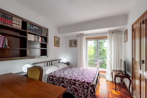 A bedroom with a bed, a desk, a bookshelf, and a window with curtains.