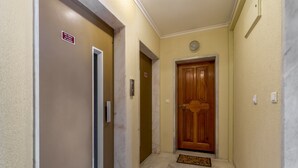 A hallway with a wooden door, a marble wall, and a doormat.
