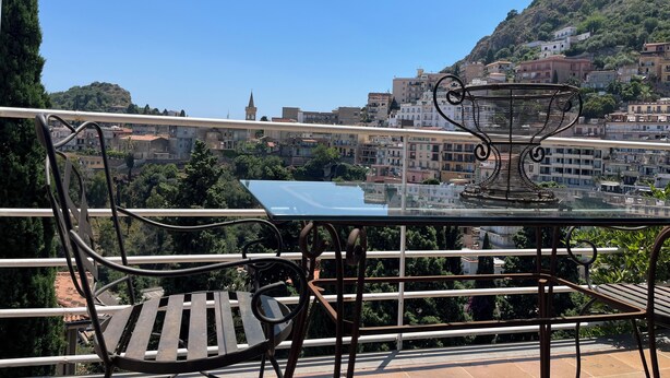 A terrace with a glass table and metal chairs, overlooking a hillside town with buildings and a church spire. - Elegant Sicilian villa in the heart of Taormina - 3 bedrooms, 3 bathrooms. (Taormina)