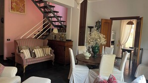 A living room with a sofa, chairs, a dining table with a vase, a staircase, and a kitchen area visible through an open door. - Elegant Sicilian villa in the heart of Taormina - 3 bedrooms, 3 bathrooms. (Taormina)