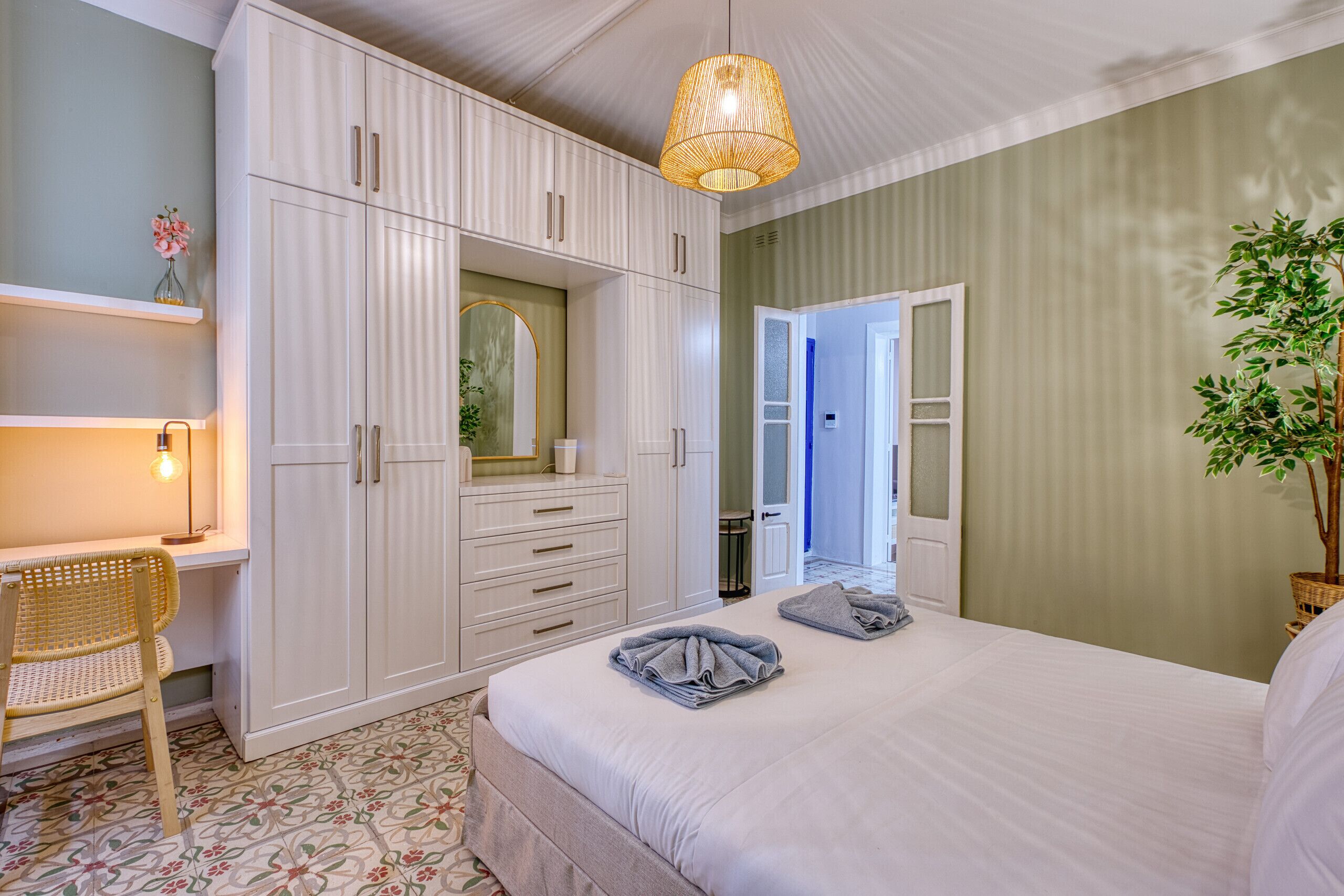 Un dormitorio con cama, armario, escritorio, silla y lámpara colgante.