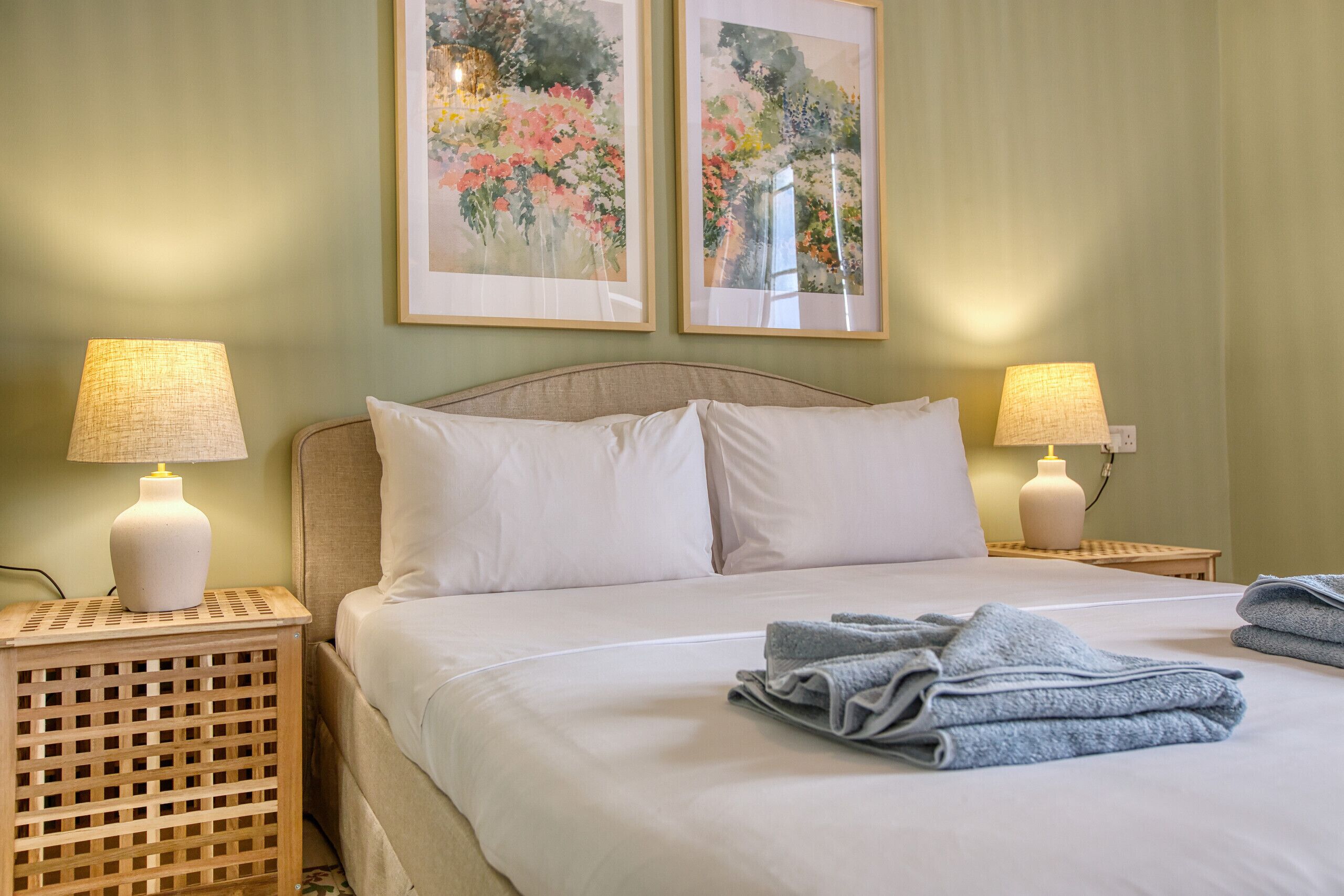 Una cama bien hecha con sábanas blancas y dos lámparas de noche en mesitas de madera.