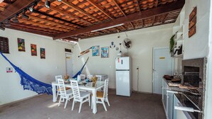 A kitchen with a white refrigerator, a dining table with chairs, and a hammock. - Casa c 4 su tes Piscina Churrasqueira e Garagem (Cabedelo)