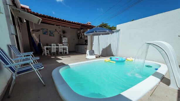 A small outdoor swimming pool with a water fountain, surrounded by lounge chairs and a covered patio area. - Casa c 4 su tes Piscina Churrasqueira e Garagem (Cabedelo)