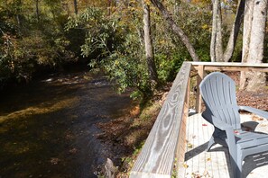 A wooden deck with a chair overlooking a river, surrounded by trees.