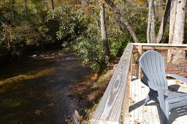 A wooden deck with a chair overlooking a river, surrounded by trees.