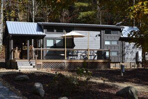 A modern cabin with a deck, outdoor seating, and a covered patio area.