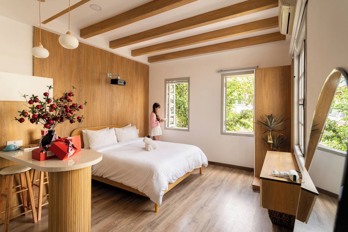 Ein modernes Schlafzimmer mit einem Bett, Holzbalken, einem Schreibtisch mit einer Vase und großen Fenstern.