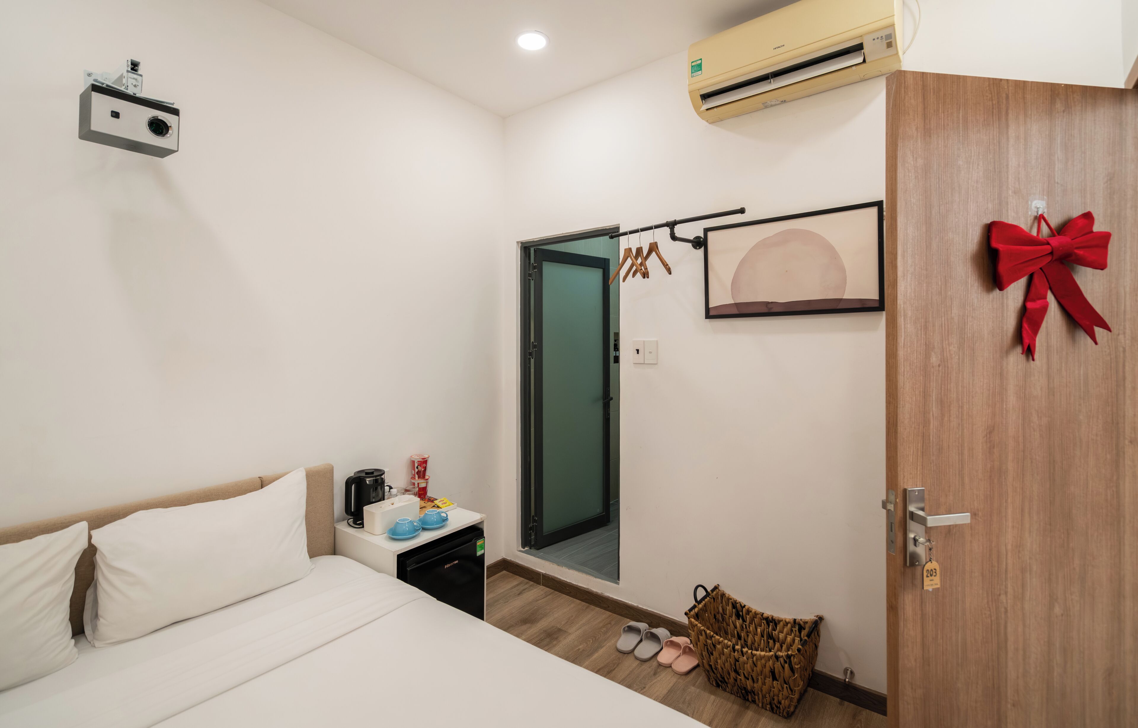 Une chambre d’hôtel avec un lit, une petite table avec une bouilloire, une machine à café, un panier et une porte décorée d’un nœud rouge.