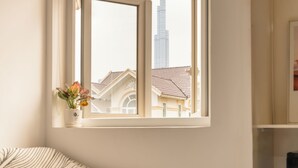 A hotel room with a bed, a window with a view of a tall building, and a bedside table with a vase of flowers. - Cham's Hotel & Homestay (Ho Chi Minh City)
