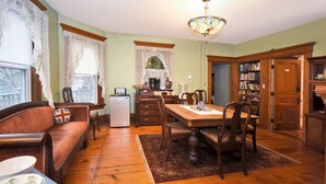 A cozy dining area with a wooden table and chairs, a refrigerator, and a bookshelf. - Balcony Room in Victorian Home private bath (Shelburne Falls)