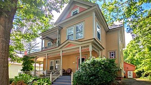 A two-story house with a front porch, a staircase leading to the entrance, and a large tree in the foreground. - Balcony Room in Victorian Home private bath (Shelburne Falls)