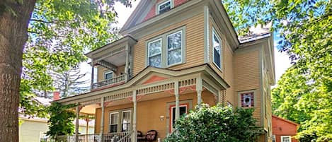 A two-story house with a front porch, a staircase leading to the entrance, and a large tree in the foreground.