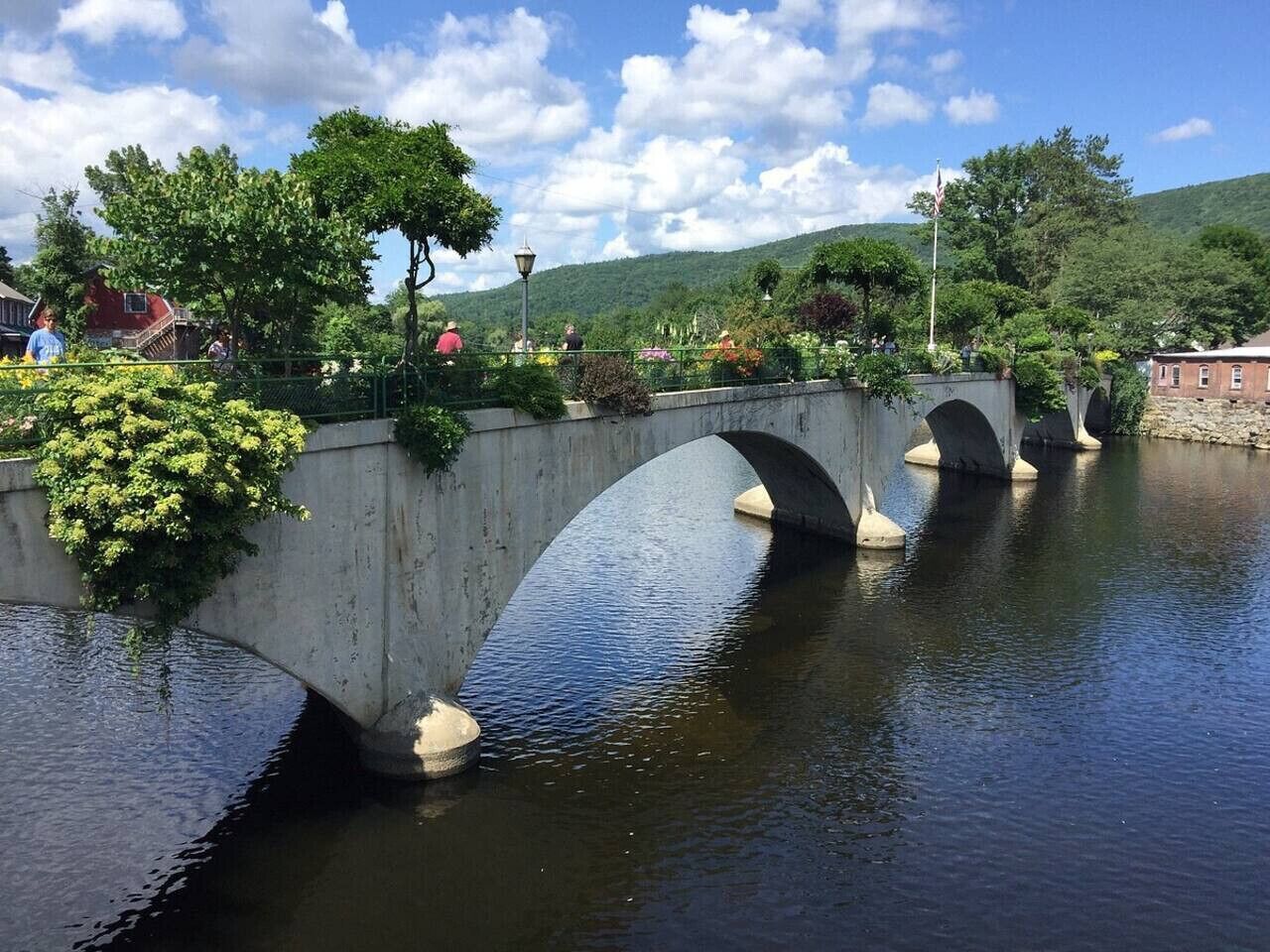 A stone bridge over a calm river with greenery on either side.