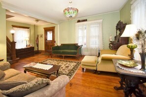 A traditional living room with a green sofa, a wooden coffee table, and a patterned rug. - Balcony Room in Victorian Home private bath (Shelburne Falls)