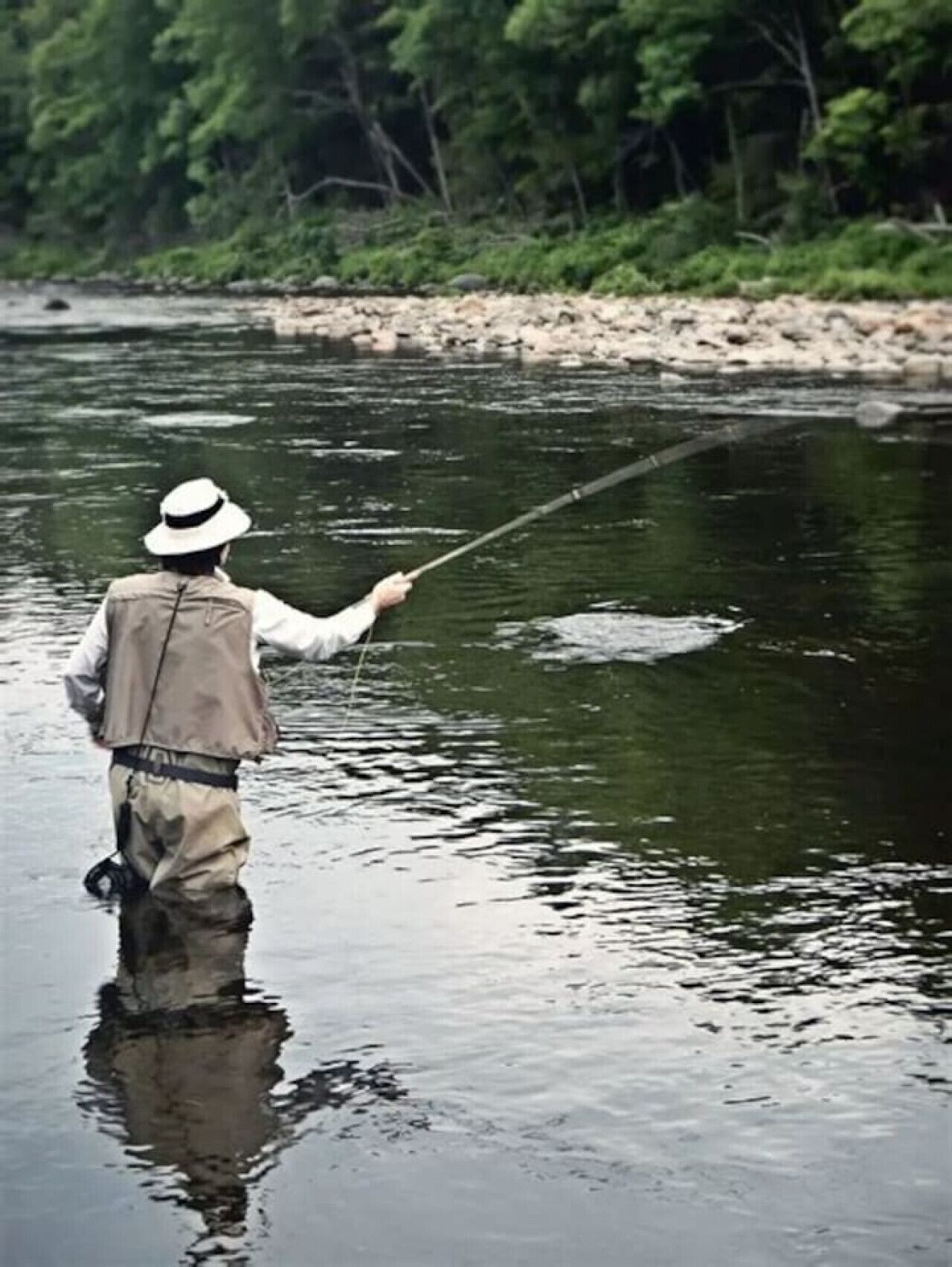 A person standing in a river, holding a fishing rod.