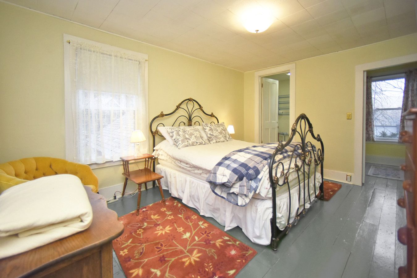 Une chambre à coucher avec un lit, une chaise, une table de chevet, une lampe et une fenêtre avec des rideaux.