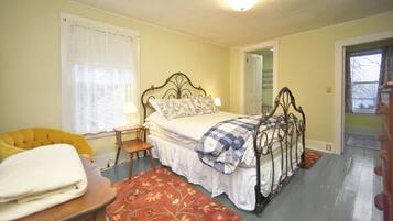 Une chambre à coucher avec un lit, une chaise, une table de chevet, une lampe et une fenêtre avec des rideaux.