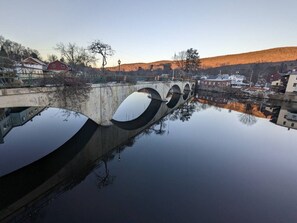Un pont enjambant une étendue d’eau calme dont le reflet est limpide, entouré d’immeubles et de collines.