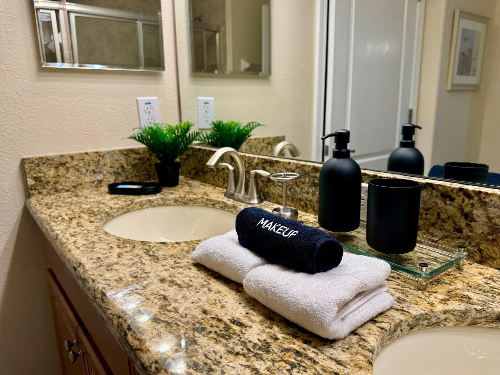 A bathroom with granite countertops, a sink, a mirror, a towel, and a black bottle.