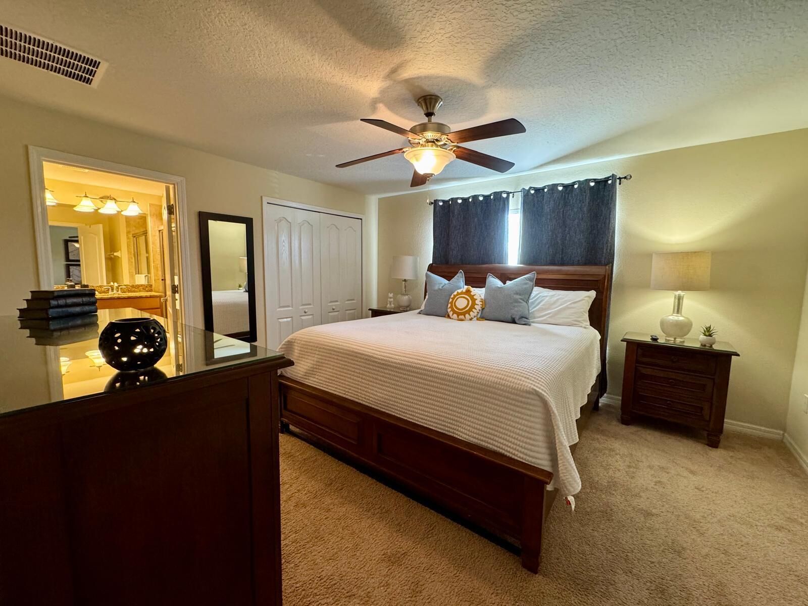 Une chambre à coucher comprenant un lit, un ventilateur de plafond, une table de chevet, une commode et un miroir.