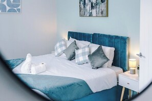 A neatly made bed with a blue headboard, white bedding, and checkered pillows.