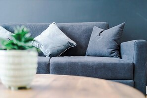 Un canapé gris avec deux coussins, un pot blanc texturé contenant des plantes vertes et une table en bois.