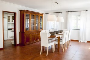 A dining area with a wooden cabinet, white chairs, a dining table, and a window with curtains. - Cottage 'Casa Dos Pinheiros' with Private Pool, Wi-Fi and Air Conditioning (Vila Nova de Santo André)