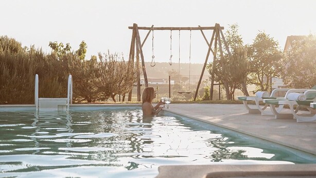 Una piscina con un columpio, sillas de descanso y vistas a árboles y colinas.