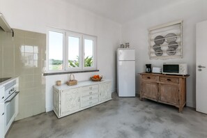 Eine Küche mit Fenster, weißen Schränken, einer Mikrowelle und einem Kühlschrank.