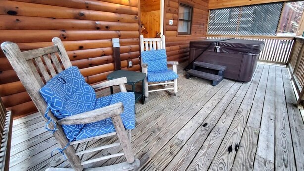 A wooden deck with a rocking chair and a table, a hot tub, and a ceiling fan.