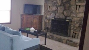 A living room with a stone fireplace, a television on a wooden cabinet, and a light blue sofa.