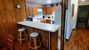 Cocina con armarios de madera, encimera blanca y dos taburetes.