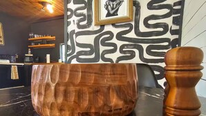 Uma tigela de madeira sobre uma bancada de mármore preto, um moedor de pimenta de madeira e uma parede com um design abstrato em preto e branco.